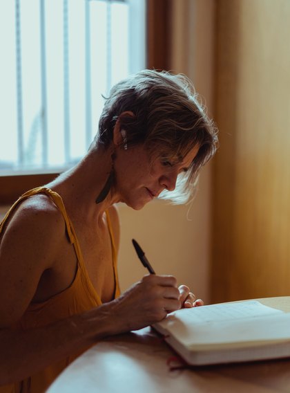 A woman writing in a notebook by a window.