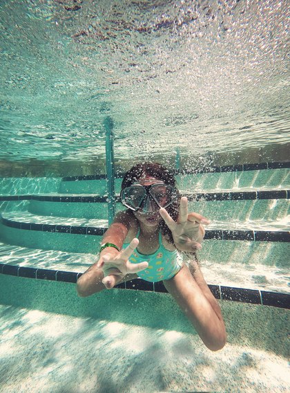 A child underwater in a pool, smiling at the camera.