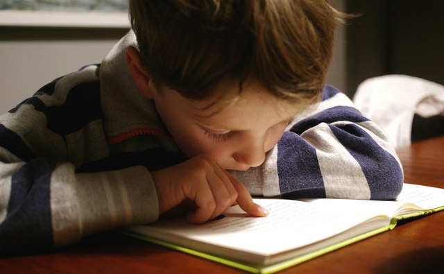 A young boy following a line of text with his finger as he reads.