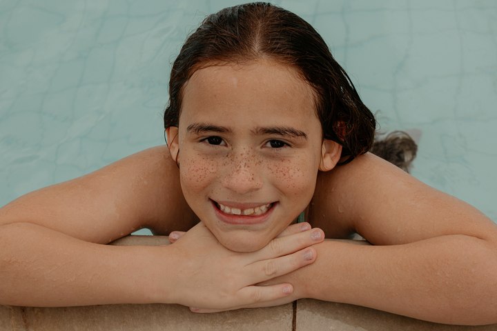 A girl resting her arms on the edge of a pool, smiling.