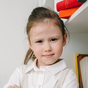 A young student standing beside a bookshelf.